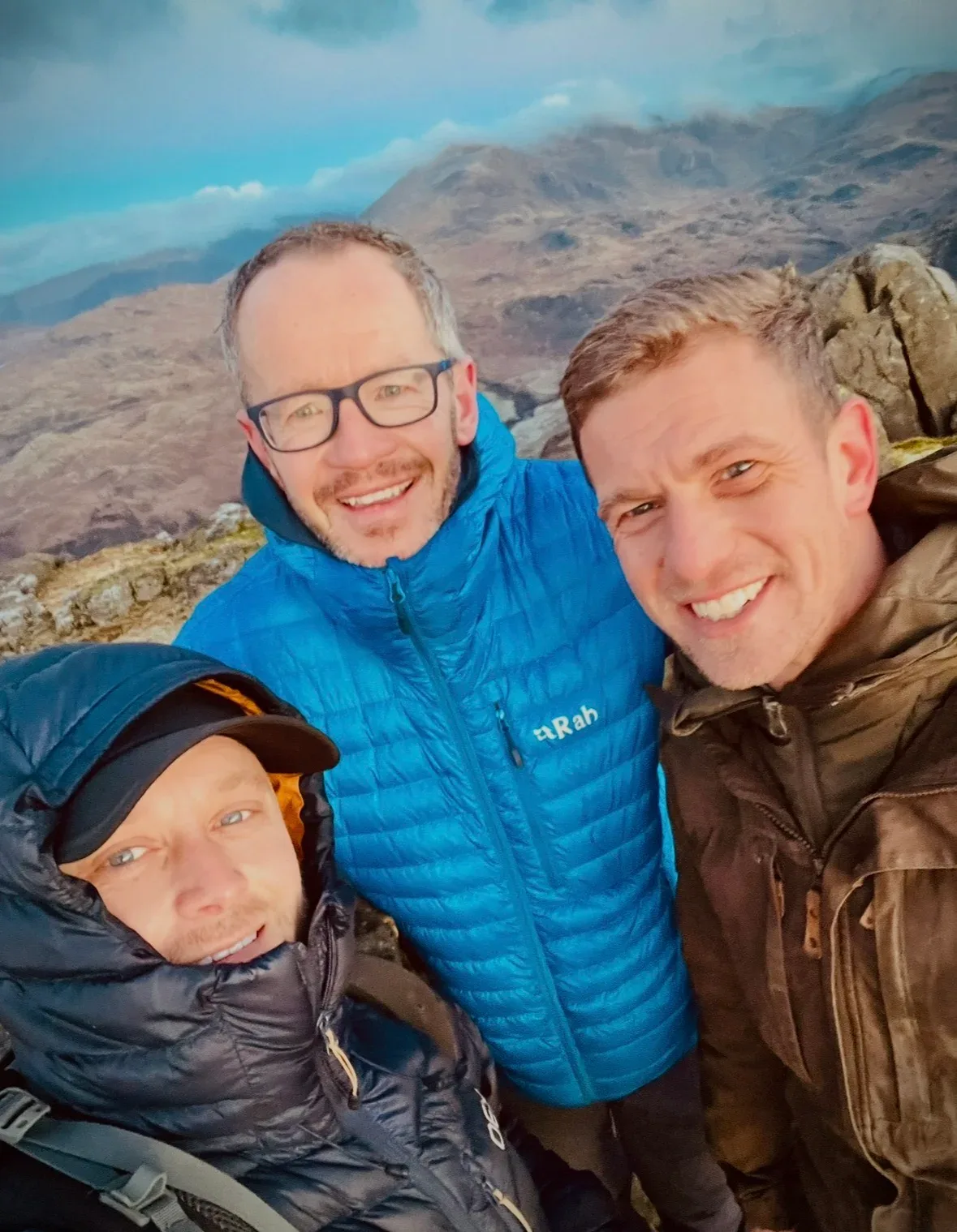 Three walkers smiling together with mountain ridges behind them