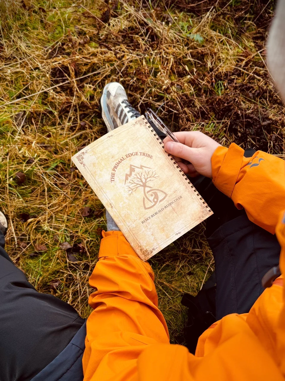 The Primal Edge Tribe booklet held outdoors by someone wearing an orange jacket