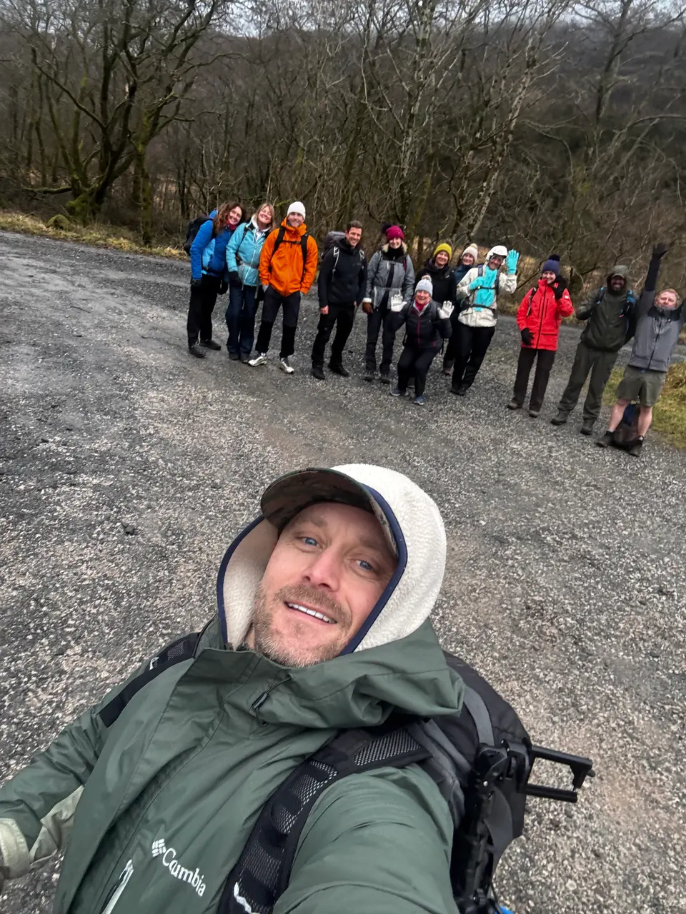 A guide takes a selfie with a walking group behind on a woodland path