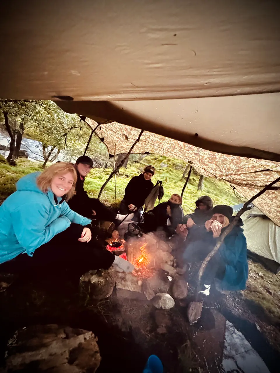 A group sheltering under a tarp around a fire